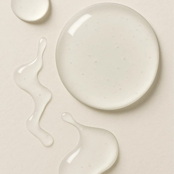 Druppels transparant huidserum op beige achtergrond, natuurlijke gezichtsverzorging
