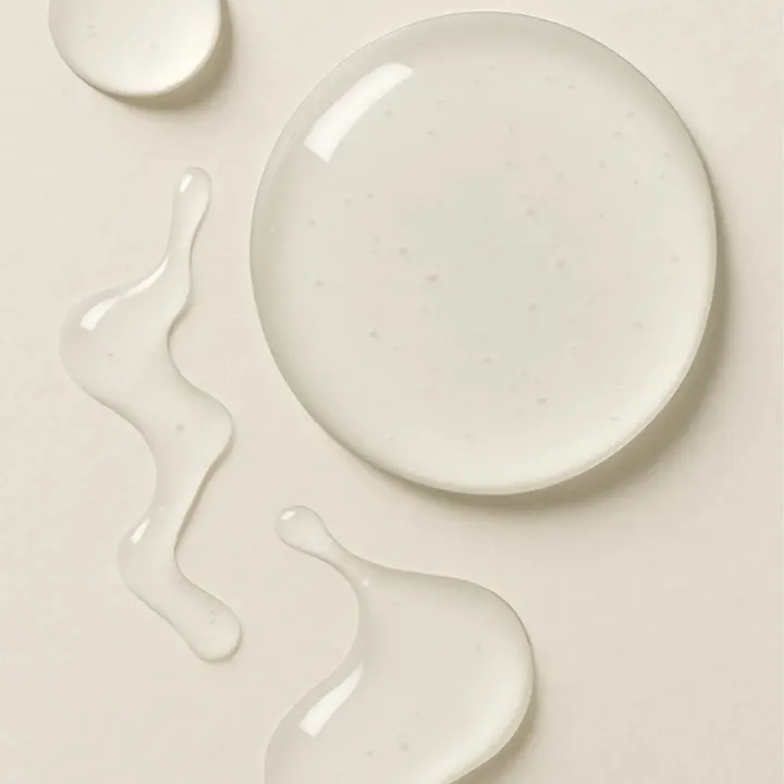 Druppels transparant huidserum op beige achtergrond, natuurlijke gezichtsverzorging